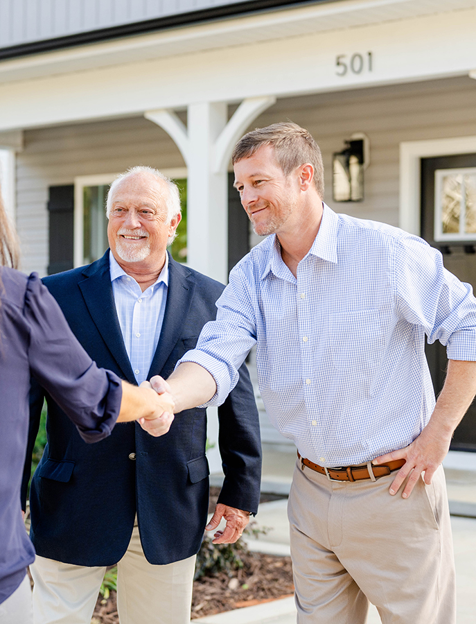 William Elmore and Billy Elmore shaking hands with a new home buyer in front of the house